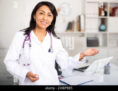 Latina Frau Arzt tragen weiße medizinische Uniform und Stethoskop Blick auf Kamera posiert in der Privatklinik Stockfoto