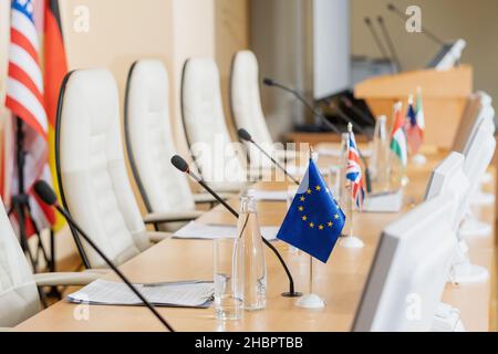 Reihe von Mikrofonen, internationalen Flaggen, Wasserflaschen, Gläsern, Computermonitoren und Papieren auf einem langen Tisch im Konferenzsaal Stockfoto