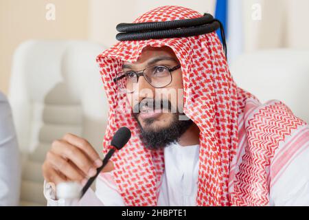 Junge, selbstbewusste Delegierte aus den Vereinigten Arabischen Emiraten spricht im Mikrofon und berichtet vor Publikum Stockfoto