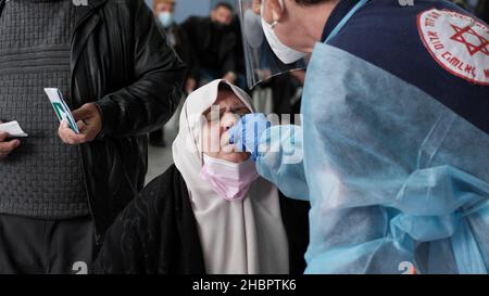 Erez Crossing, Israel. 2nd Dez 2021. Ein Sanitäter des Magen David Adom, des nationalen medizinischen Notdienstes Israels, sammelt am 20. Dezember 2021 am Grenzübergang Erez, Israel, eine Abstrichprobe einer palästinensischen Frau, bevor sie aus dem Gazastreifen nach Israel einreist, in einer mobilen COVID-19-Teststation an der Grenze zwischen Gaza und Israel. Israel hat Reisen in und aus mehreren Ländern aufgrund der COVID-19 Omnicron-Variante verboten. Israelis, die in das Land zurückkehren, müssen unabhängig vom Impfstatus in Quarantäne gehen. Kredit: Eddie Gerald/Alamy Live Nachrichten Stockfoto