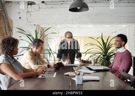 Eine Gruppe junger zeitgenössischer Mitarbeiter traf sich zu einem Start-up-Treffen, bei dem neue Ideen und Strategien am Tisch diskutiert wurden Stockfoto