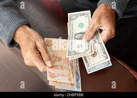 Ältere faltige Hände halten amerikanische US-Währung und türkische Lira Geschäfts- oder Wirtschaftskrise Konzept mit Dollar-Banknoten. Stockfoto