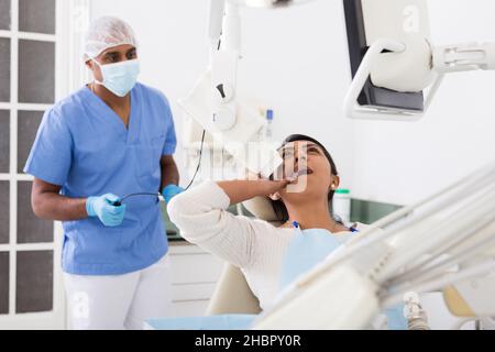 Zahnarzt, der Zähne Radiographie zu hispanischen weiblichen Patienten im Stuhl in der Zahnmedizin Büro liegen Stockfoto