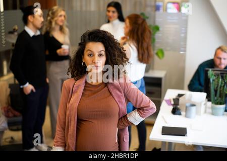 Porträt einer Schwangeren Geschäftsfrau mit Kollegen im Hintergrund im Büro Stockfoto