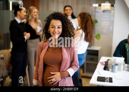 Porträt einer lächelnden, Schwangeren Geschäftsfrau mit Kollegen im Hintergrund im Büro Stockfoto