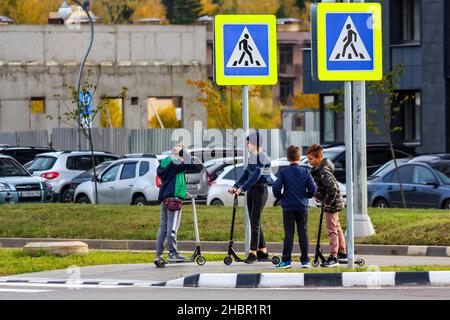 Obninsk, Russland - 2. Oktober 2019: Eine Gruppe von Kindern auf einem Kick Scooter an einer Fußgängerüberfahrt über eine Autobahn. Verkehrsinselet Stockfoto