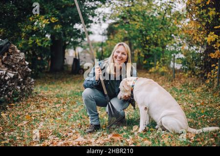 Lächelnde reife Frau mit Hund, der in den Hinterhof schaut Stockfoto