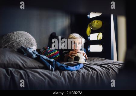 Beschaulicher Junge mit Fußball, der zu Hause auf dem Bett liegt Stockfoto