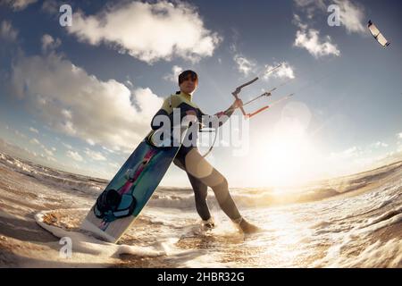 Charakterzug eines professionellen Surfers, der am Strand mit Kite und Wakeboard steht. Kite-Surfing-Konzept, Spaß im Meer Stockfoto
