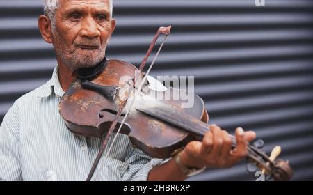 Teilweise Nahaufnahme eines älteren Mannes mit nachdenklichem Gesichtsausdruck, der mit einer Geige, die er in der Hand hält, eine Melodie aufführt. Stockfoto