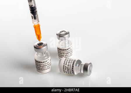 Turin, Italien - 18. Dezember 2021: Pfizer-BioNTech COVID-19-Impfstoff Comirnaty-Fläschchen, drei Fläschchen mit Spritze, die Impfstoffdosis ansaugt, dritte Dosis Conce Stockfoto