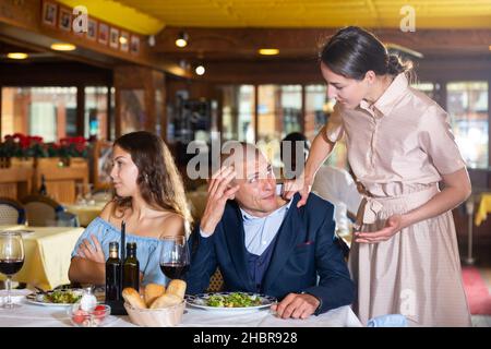 Freundin trifft untreuen Mann, der Zeit mit einer anderen Frau im Restaurant verbringt Stockfoto