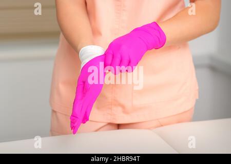 Die Hand der Kosmetikerin legt sterile rosa Handschuhe an und bereitet sich darauf vor, die Kunden im Haus zu empfangen Stockfoto