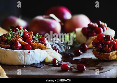 Gebackenen Camembert Brie Käse mit Cranberry, Honig, Balsamico-Essig und Nuss genießen und mit Thymian garniert. Serviert mit gerösteten Brotscheiben. Stockfoto