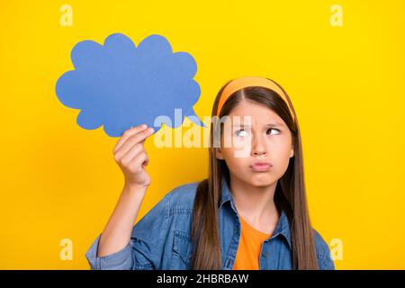 Foto von zweifelhaft unsicher preteen Mädchen gekleidet Jeans Hemd halten Sprechblase suchen leeren Raum isoliert gelbe Farbe Hintergrund Stockfoto