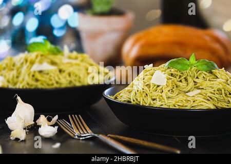 Selektiver Fokus auf zwei Platten Pesto-Spaghetti-Pasta mit frischen Basilikumblättern und Parmesan-Käse auf einem schwarzen rustikalen Holztisch. Stockfoto