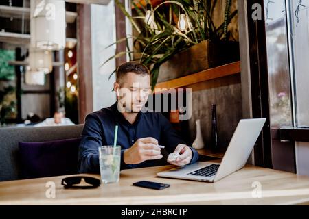 Serious Geschäftsmann hat Online-Meeting auf Laptop im Restaurant. Remote-Arbeit. Stockfoto