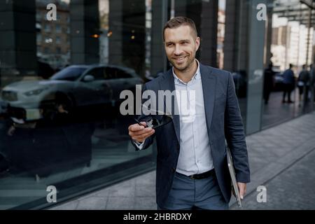 Der erfolgreiche junge Geschäftsmann im Anzug lächelt und geht auf der Straße Stockfoto