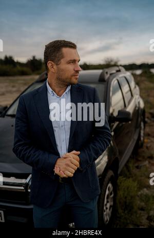 Porträt eines Geschäftsmannes mit schwarzem Oldtimer-Anzug. Der Mensch steht in der Nähe seines Autos im Freien. Stockfoto