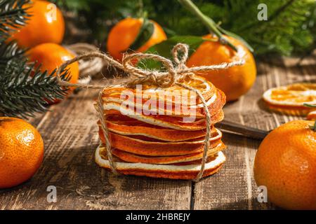 Trockene Orangen Scheiben Snack. Getrocknete Zitrusfrüchte für Weihnachtsdekorationen. Mandarinen mit Blättern, Tannenzweigen, Schere und Faden. Holzrückenboden Stockfoto