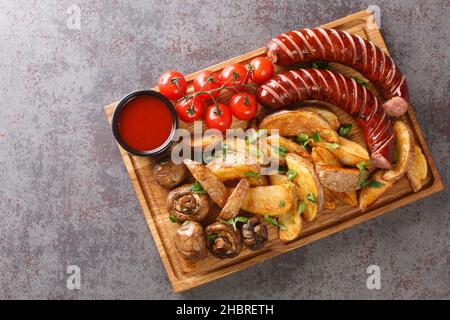 Gebratene Würstchen im rustikalen Stil mit Kartoffeln und Pilzen und heißer Soße aus der Nähe auf einem Holztablett auf dem Tisch. Horizontale Ansicht von oben Stockfoto