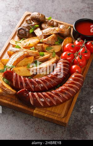 Gegrillte Würstchen mit Kartoffelkeilen und Pilzen aus der Nähe auf einem Holztablett auf dem Tisch. Vertikal Stockfoto