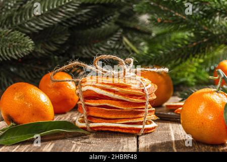 Trockene Orangen Scheiben Snack. Getrocknete Zitrusfrüchte für Weihnachtsdekorationen. Mandarinen mit Blättern, Tannenzweigen, Schere und Faden. Holzrückenboden Stockfoto
