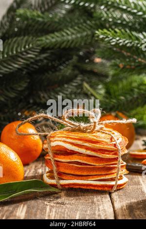 Trockene Orangen Scheiben Snack. Getrocknete Zitrusfrüchte für Weihnachtsdekorationen. Mandarinen mit Blättern, Tannenzweigen, Schere und Faden. Holzrückenboden Stockfoto