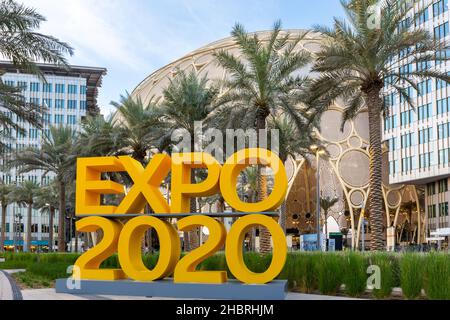 Dubai, VAE, 09.12.2021. Gelbes Logo der Expo 2020 auf der Expo 2020 Dubai mit Al Wasl Plaza und Palmen im Hintergrund. Stockfoto