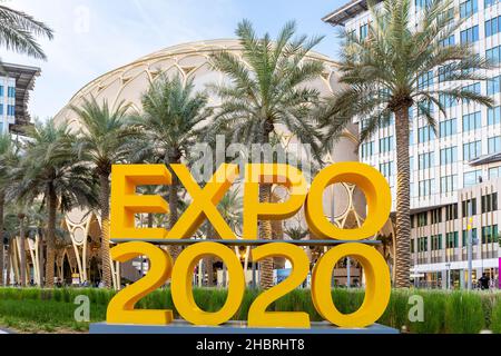 Dubai, VAE, 09.12.2021. Gelbes Logo der Expo 2020 auf der Expo 2020 Dubai mit Al Wasl Plaza und Palmen im Hintergrund. Stockfoto