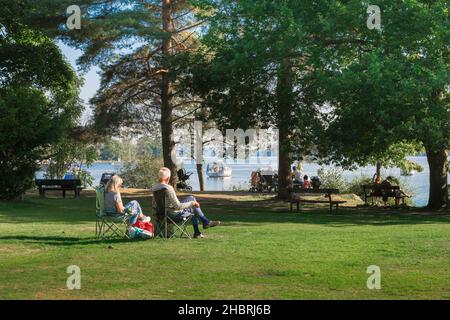 Seniorenpaar, Rückansicht im Sommer eines Seniorenpaares, das auf Lagerstühlen sitzt und einen Blick auf Lake Windermere, Cumbria, England, UK, genießt Stockfoto