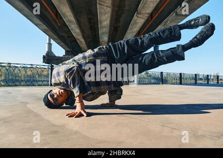 Junger Mann bricht Tänzer tanzen auf städtischen Hintergrund akrobatische Stunts Durchführung. Straßenkünstler beim Breakdance im Freien Stockfoto