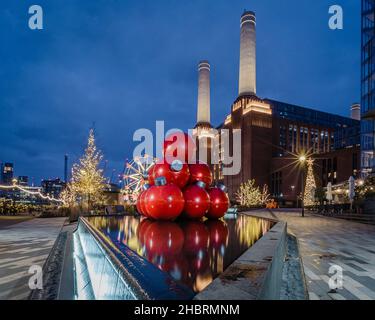 Riesige rote Kugeln im Brunnen und andere Attraktionen im Winter Village by Battersea Power Station in London. Stockfoto