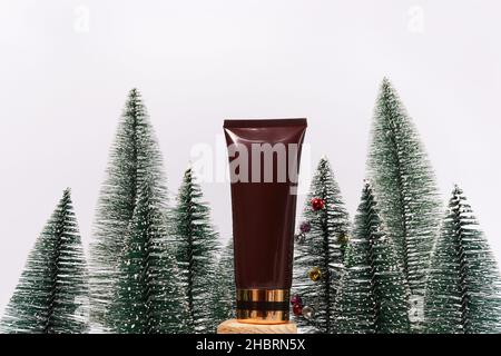 Gesichtscreme oder Körpercreme mit Goldkappe und Tannenbäumen auf weißem Hintergrund. Mockup mit Kopierbereich. Flasche zum Branding, Fron Stockfoto