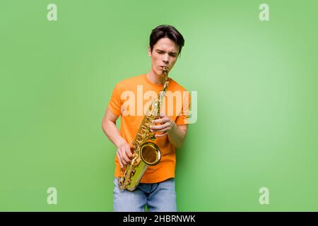 Foto von positiven kreativen glücklich jungen Mann halten Hände spielen Saxophon isoliert auf grünem Hintergrund Stockfoto