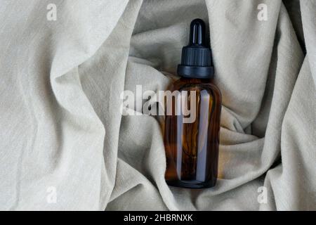 Glasflasche mit einer Pipette auf einem Hintergrund aus Leinentuch, Draufsicht. Eine braune Flasche ätherisches Öl. Kosmetische Glasbehälter. Pflanzenöl in a b Stockfoto