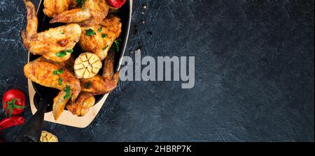 Gegrillte Hähnchenflügel auf einer gusseisernen Pfanne auf einem schwarzen ovalen Steinhintergrund. Draufsicht. Selektiver Fokus. Stockfoto