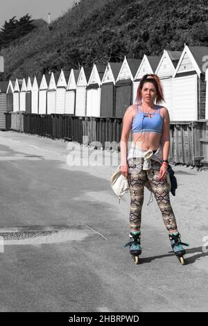 Junge Frau Rollschuhe auf Rollschuhe Rollschuhe Schaufeln auf Promenade von Strandhütten in Bournemouth, Dorset UK im April Stockfoto