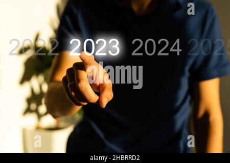 Fingerdruck der blauen Start 2023-Taste auf der virtuellen Benutzeroberfläche auf grauem Hintergrund mit Platz für Text. Konzept des neuen Jahres. Businessman Pressing Stockfoto