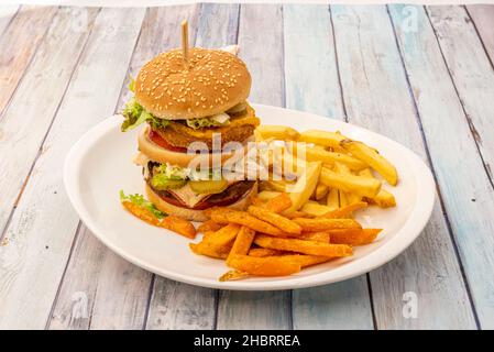 Toller und sehr schöner doppelter Burger mit knusprigem Huhn und Rindfleisch mit Zwiebeln, viel Speck, Cheddar-Käse und Tomaten mit Salat und Mayonnaise, Pommes und Stockfoto