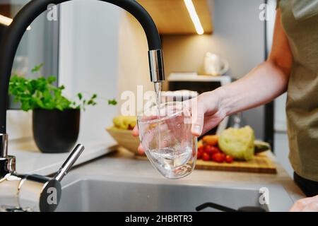 Frau goss Wasser aus dem Wasserhahn in das Glas in der Küche Stockfoto
