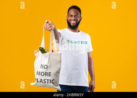 African American Volunteer Guy Zeigt Weiße Einkaufstasche, Gelber Hintergrund Stockfoto