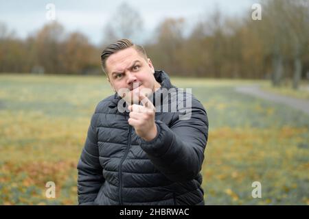 Streitlustig aggressiver junger Mann, der den Zuschauer bedroht und mit einem bärigen Blendlicht auf den Finger zeigt Stockfoto