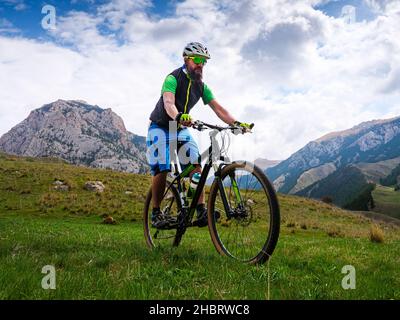 Der Radfahrer fährt an einem Sommertag in den Bergen. Bärtiger Sportler auf einem Mountainbike. Aktivitäten im Freien Stockfoto