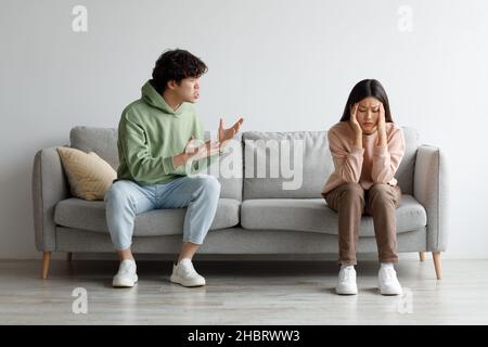 Missverständnisse in Beziehungen. Millennial asiatisches Paar streitete zu Hause auf der Couch, Mann schrie seine Frau an Stockfoto