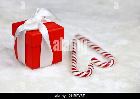 Rote Geschenkbox mit weißer Schleife und Weihnachtsbonbons auf dem Pelzteppich. Romantisches Geschenk für Neujahr oder Valentinstag Stockfoto