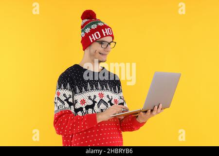 Mann in Weihnachts-Pullover mit Laptop auf gelbem Hintergrund Stockfoto