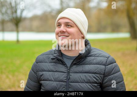 Hypnotisierter junger Mann, der mit einem Lächeln aufschaut, wenn er sich amüsiert, während er draußen in einem Park zuschaut Stockfoto