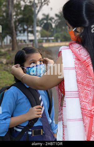 Ein indisches Schulkind, das nach einer Pandemie wieder zur Schule geht, wobei ihre Mutter Nasenmaskenschutz trägt Stockfoto