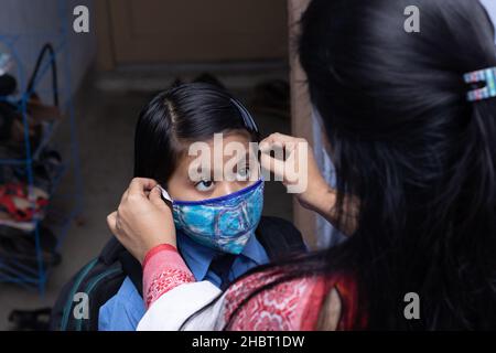 Eine indische Mutter bereitet ihr Mädchen mit Nasenmaskenschutz vor, um es nach einer Pandemie in die Schule zu schicken Stockfoto